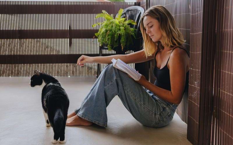 A woman sitting on a patio reading with her cat.